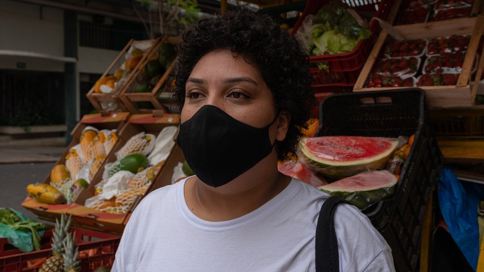 Franciele de máscara contra a covid-19, em frente a banca de frutas