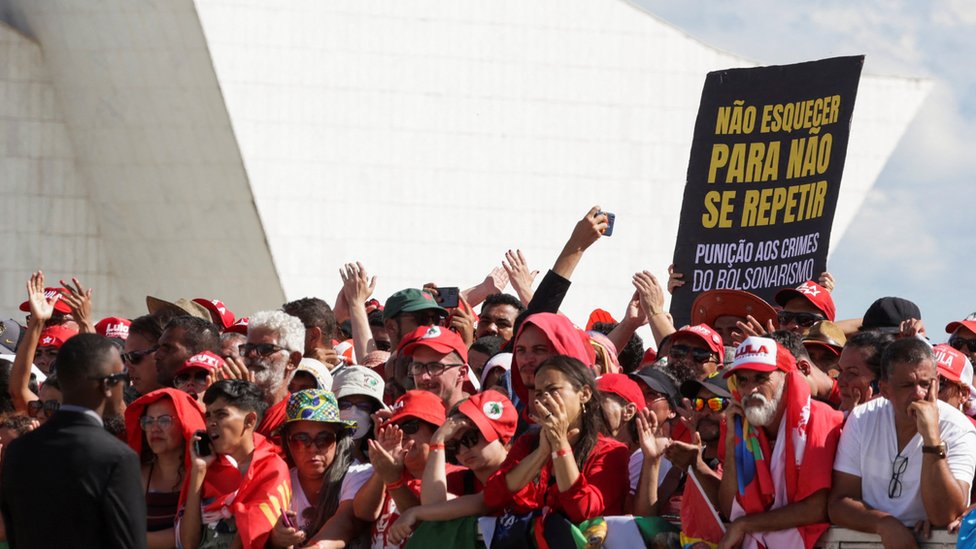 Dezenas de apoiadores em área externa de Brasília, com cartaz dizendo: 