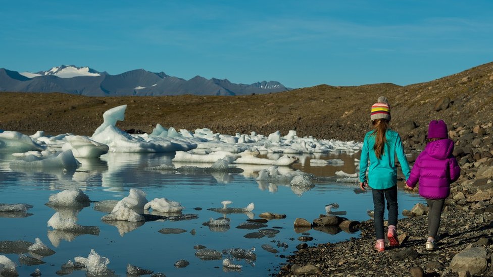 İzlanda'da eriyen buzulların kenarında yürüyen iki çocuk.