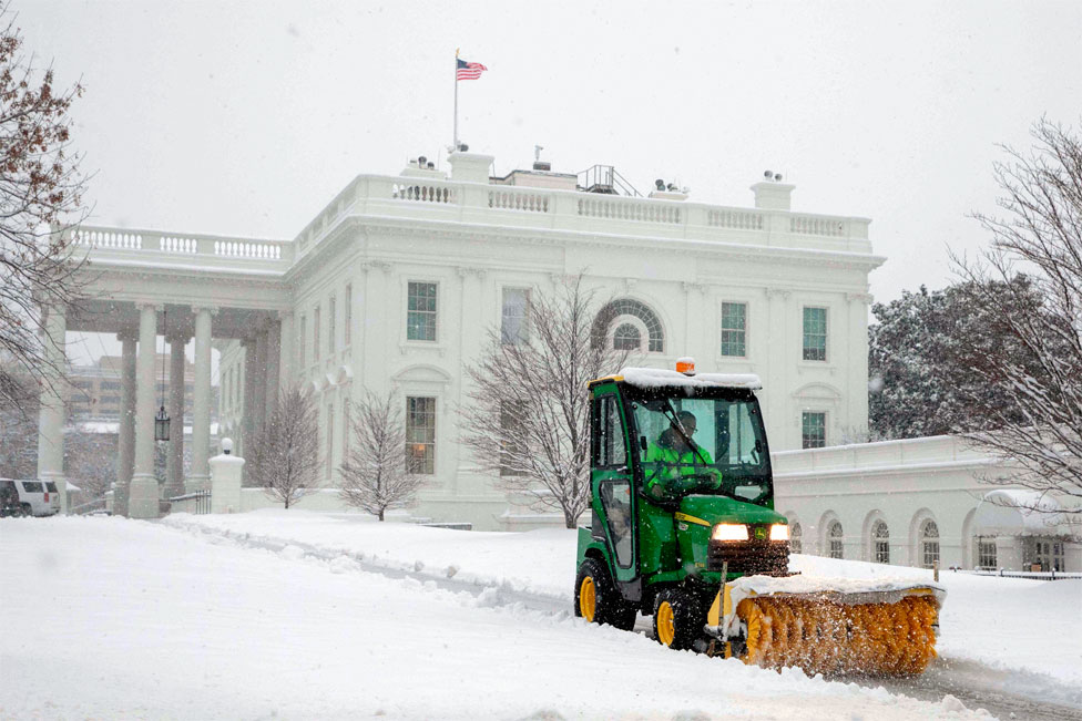 A vehicle clears snow to create a path next to the White House