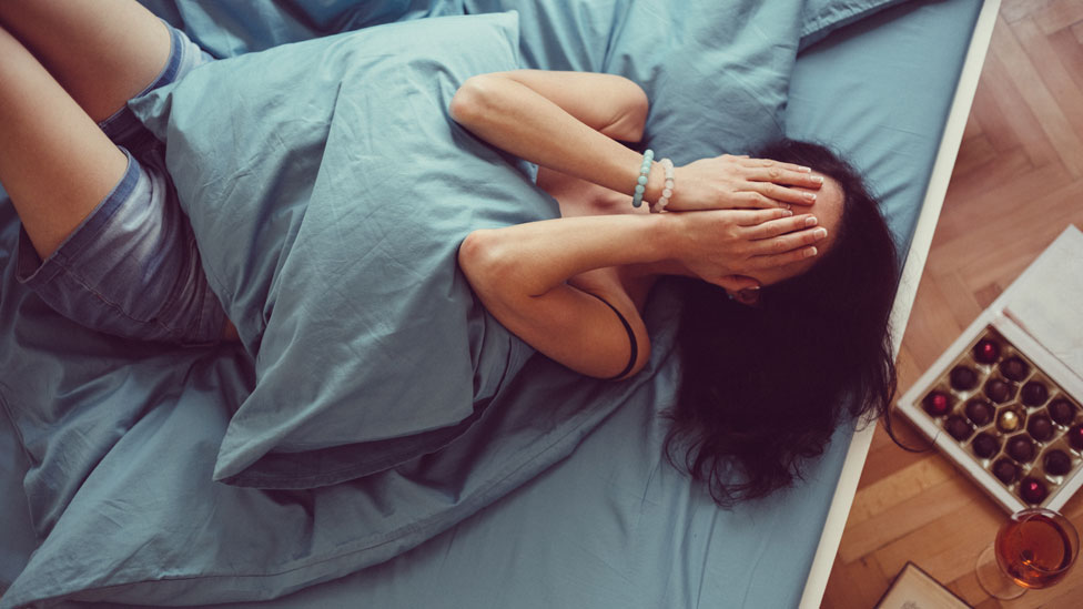 Mujer se tapa la cara en la cama.