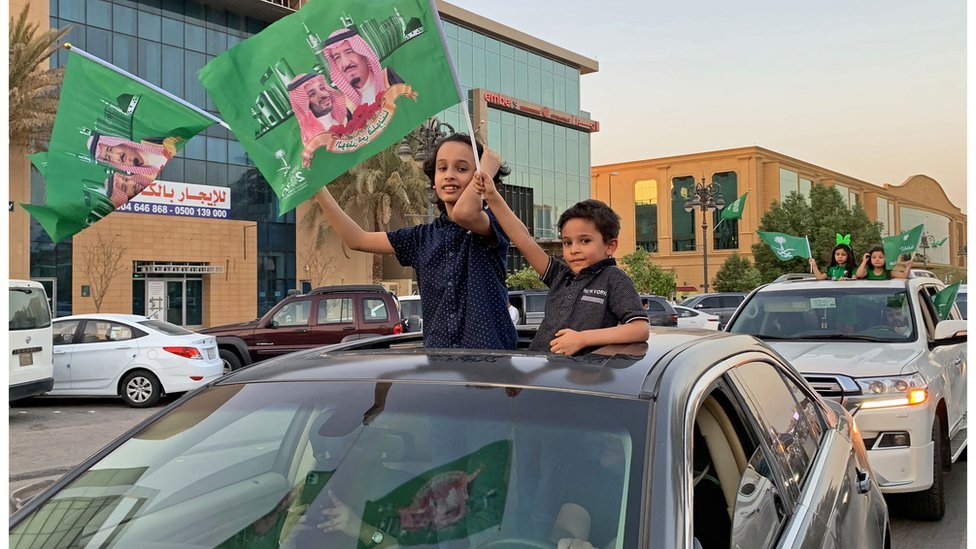 أطفال يلوحون بأعلام سعودية من نوافذ سيارات