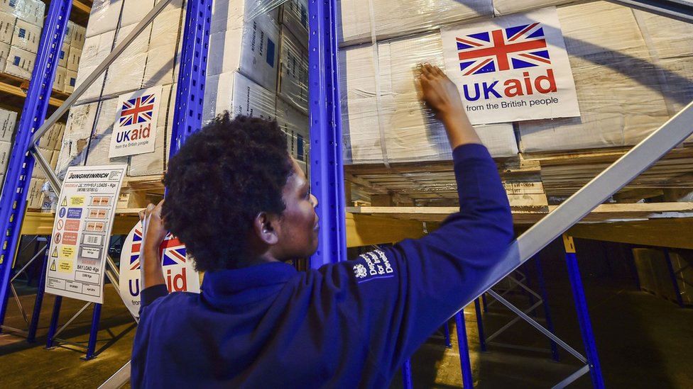 Архивная фотография от августа 2014 года, на которой офицер логистики наклеивает наклейки UK Aid на грузовые поддоны с британской гуманитарной помощью, предназначенной для районов, пострадавших от гуманитарного кризиса
