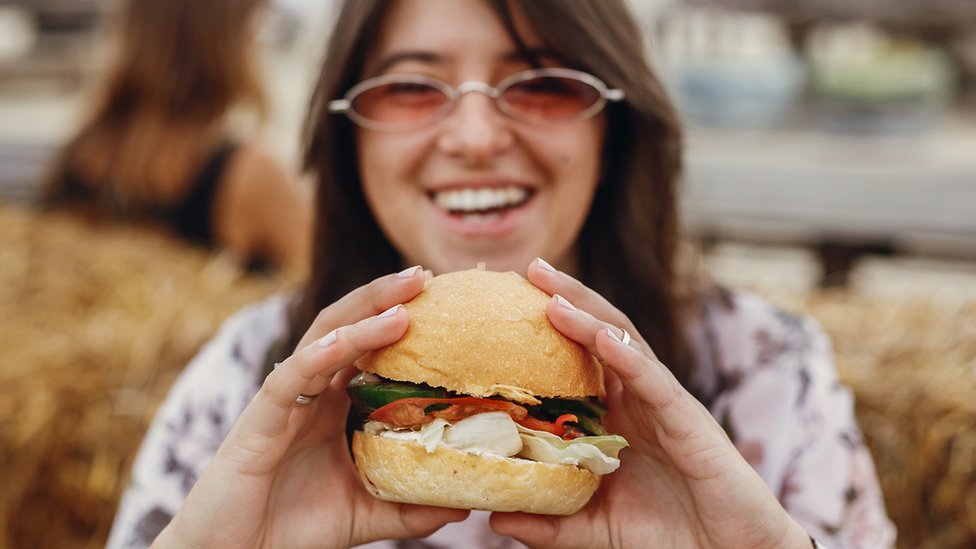 Mujer joven sosteniendo hamburguesa.