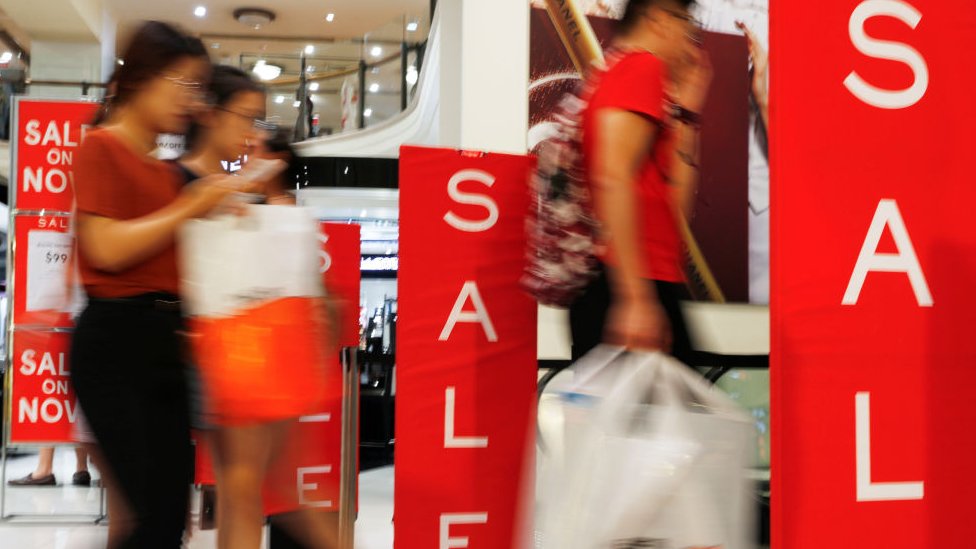 Покупатели проходят мимо вывески с распродажами в универмаге в Сиднее