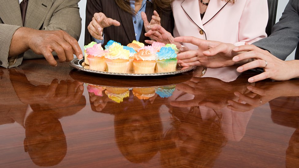 Personas rodeando una mesa con pasteles.