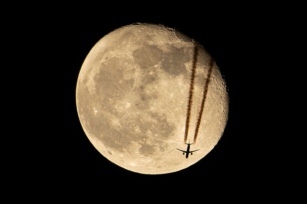 طائرة تحلق فوق البصرة ، في جنوب العراق ، مظللة أمام تراجع القمر في 18 أبريل/نيسان 2022