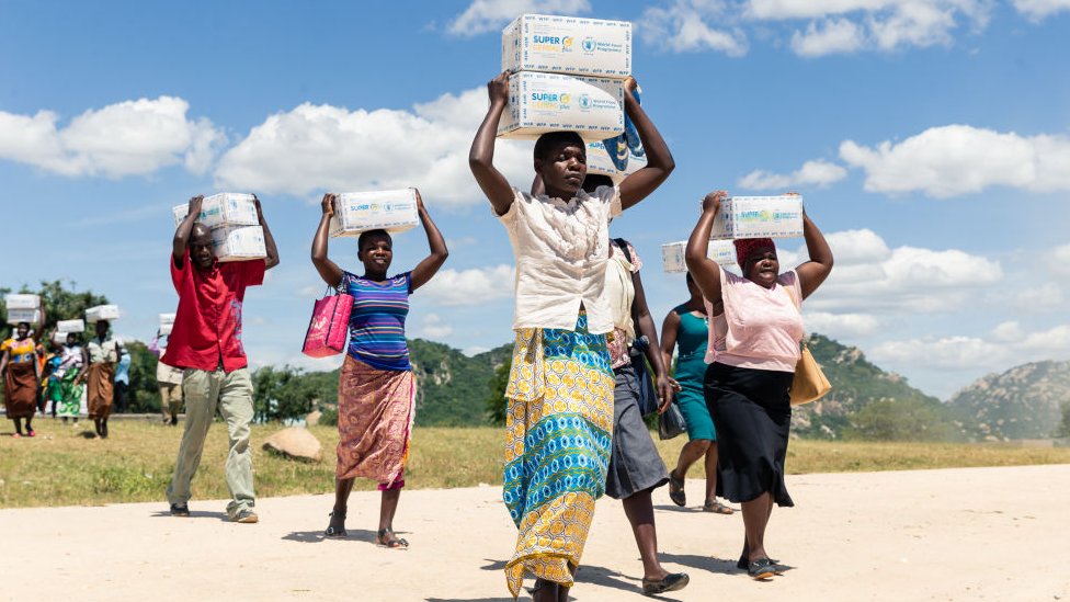 Женщины несут коробки с кашей для своих детей 13 марта 2019 года в сельском районе Мутоко в Зимбабве