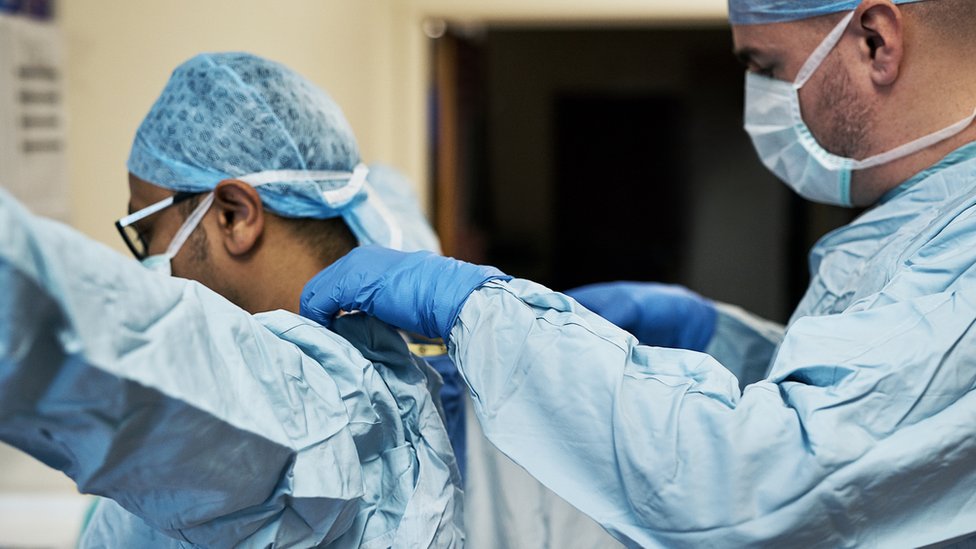 Один медицинский работник помогает другому одеть СИЗ