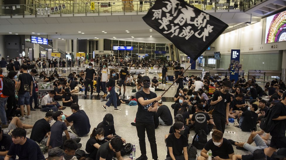 Протестующий машет черным флагом в международном аэропорту Гонконга во время антиправительственной акции протеста.