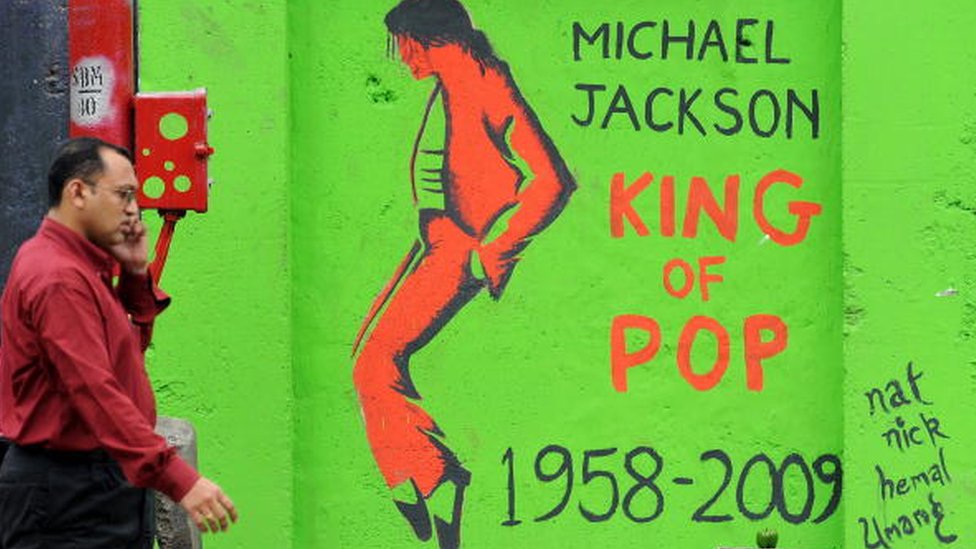 Индийский пешеход разговаривает по сотовому телефону, проходя мимо графитти с изображением покойного «короля поп-музыки» Майкла Джексона на стене в Мумбаи 28 августа 2009 г.