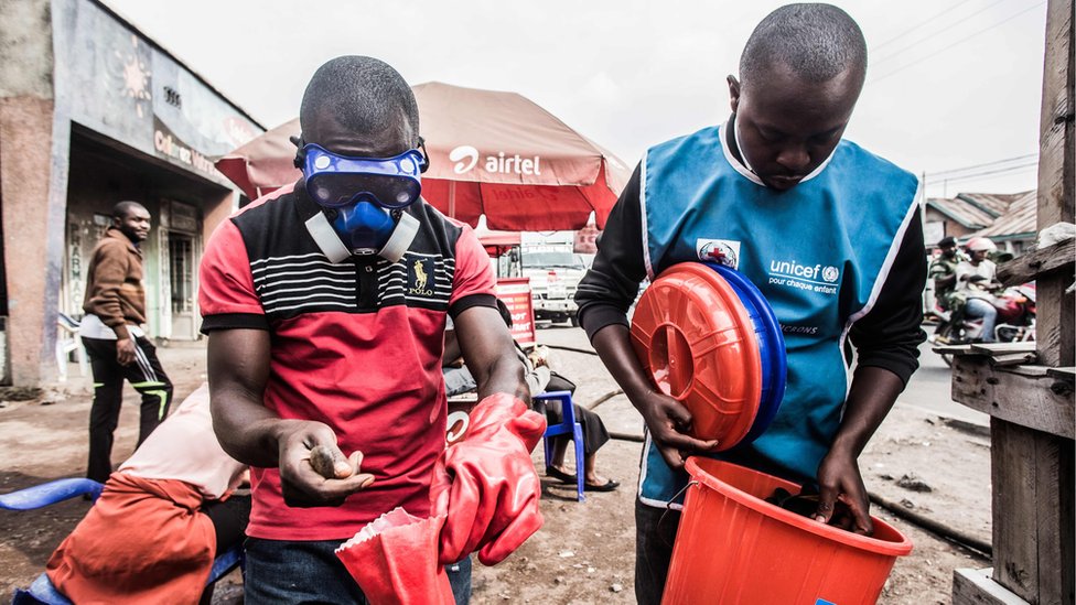 Медицинские работники носят защитную одежду для смешивания воды и хлора в Гоме