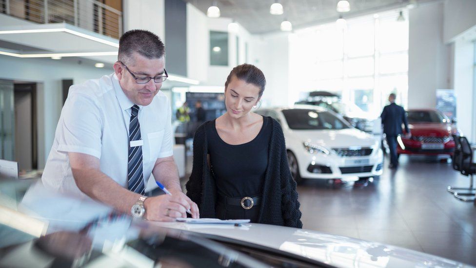 A woman and a salesman at a car showroom