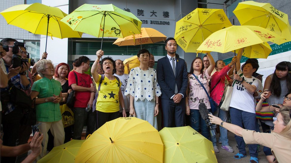 Активист за демократию Кен Цанг (справа в центре, в костюме) у магистратского суда города Коулун в сопровождении толпы сторонников, многие из которых несут желтые зонтики, перед тем, как предстать перед судом на суде 26 мая 2016 года в Гонконге.