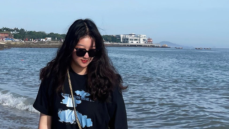 Miss Zhu wearing sunglasses by the sea or a lake and looking downwards