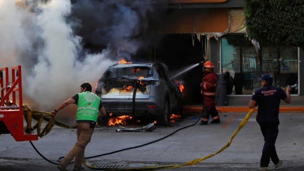 Пожарные работают над горящей машиной возле магазина после операции сил безопасности по борьбе с организованной преступностью в Селайе, штат Гуанахуато, Мексика 20 июня 2020 г.
