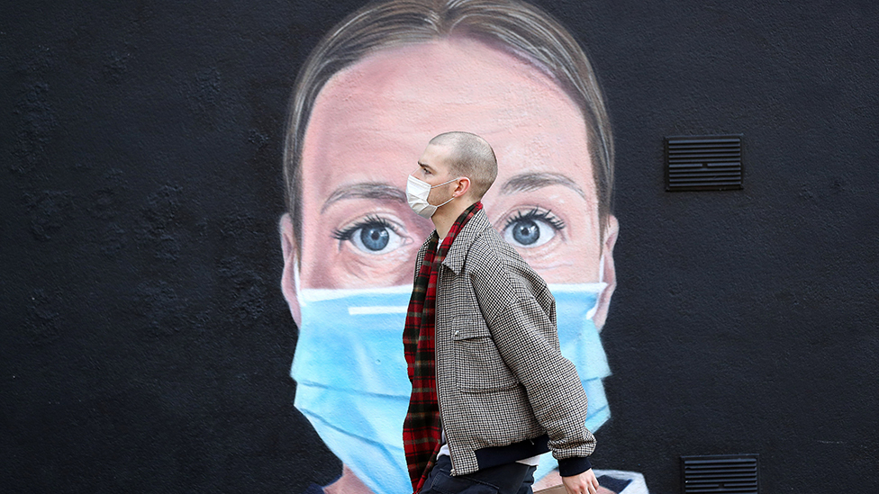 Man wearing a mask walks past a mural