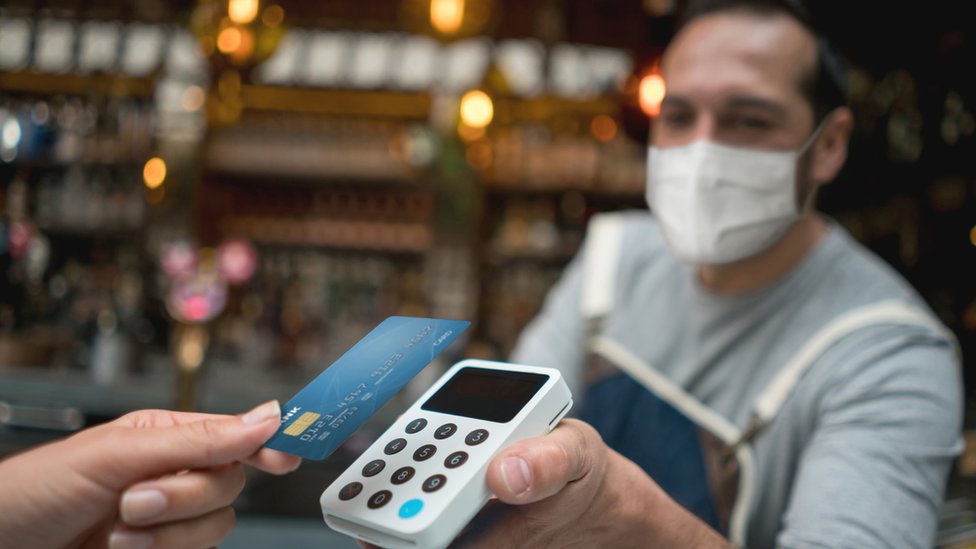 Waiter wearing a facemask while getting a contactless payment at a restaurant - stock photo