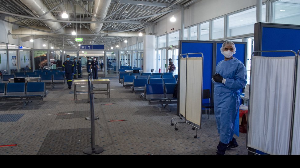 Медицинский персонал ждет, чтобы провести обследование пассажиров, прибывающих в международный аэропорт Элефтериос Венизелос в Афинах
