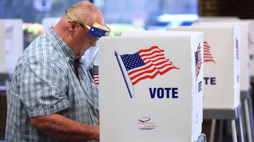 A man in a face shield casts his vote