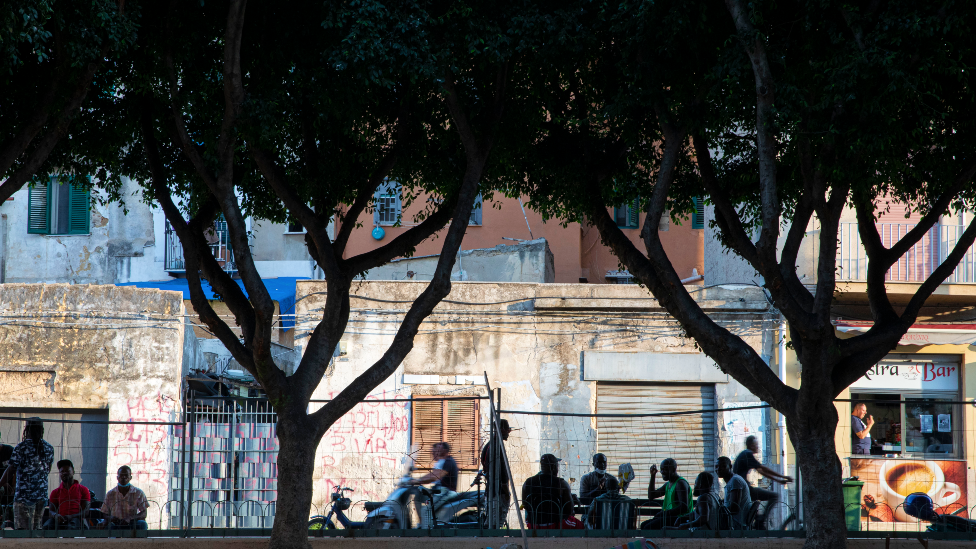 Мигранты сидят за столиками на улице в районе Балларо в Алермо - Сицилия