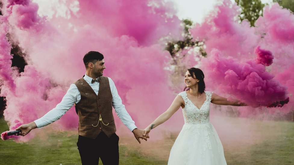 Супружеская пара позирует для свадебного фото на фоне розовых дымовых шашек
