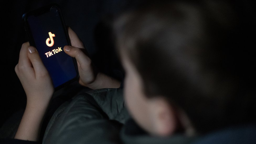 A young boy holds a smartphone loading tiktok