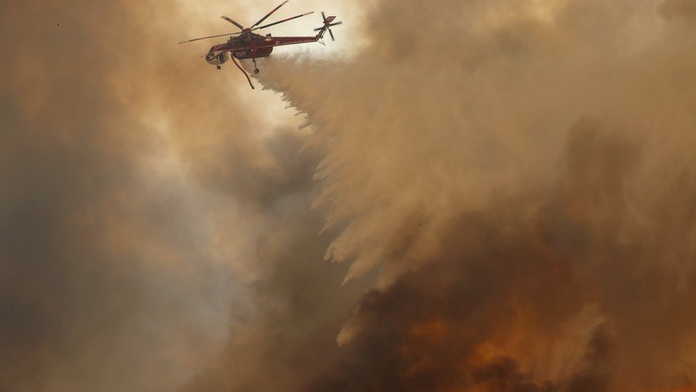 Вертолет сбрасывает воду на порожденный ветром лесной пожар в Ориндж, Калифорния