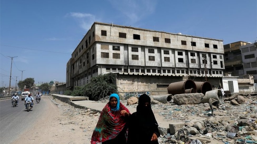 Женщины идут по дороге с заброшенным зданием швейной фабрики на заднем плане, где более 260 человек погибли в результате пожара в 2012 году в Карачи, Пакистан, 17 сентября 2020 года.