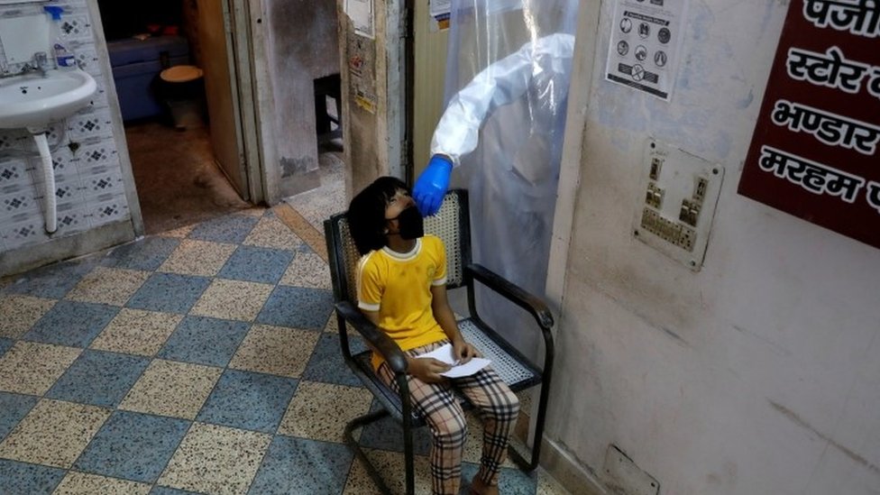 Медицинский работник в средствах индивидуальной защиты собирает образец, используя мазок у девочки в медицинском центре для проведения анализов в Дели, 27 июня