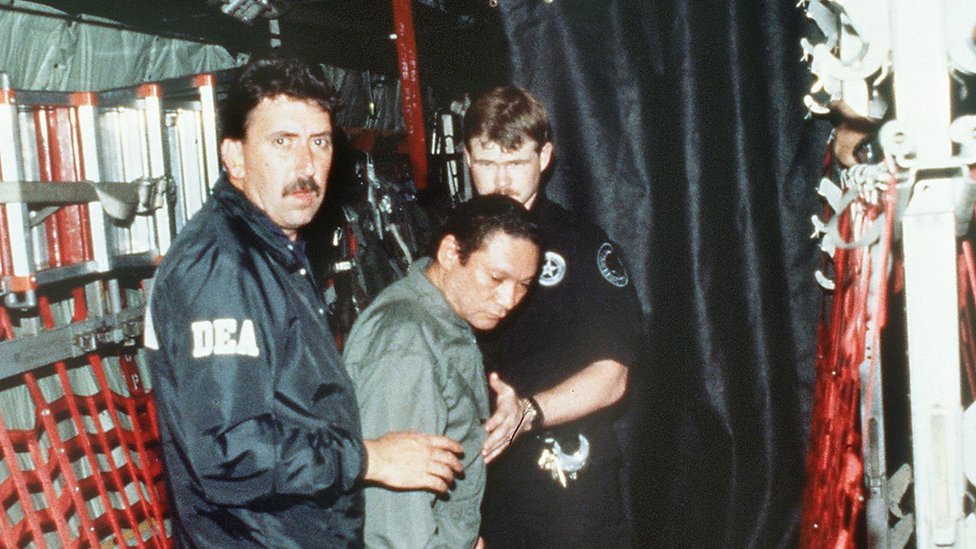 Панамский генерал Мануэль Норьега (в центре) доставлен на борт военного самолета США 3 января 1990 года для полета в Майами после ареста.
