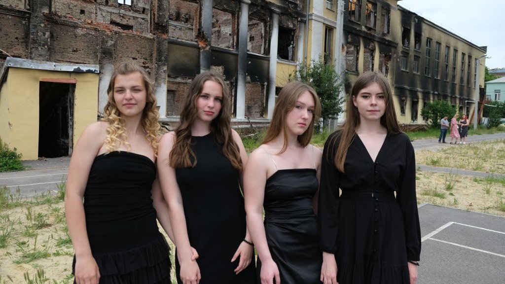 Four female students in front of their school ruins