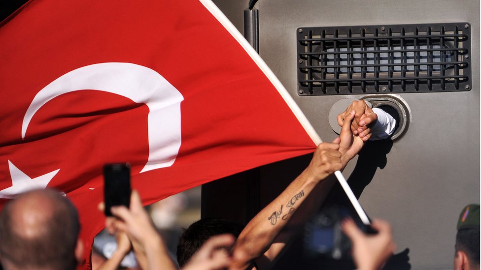 2013 yılından, bir Ergenekon davası sanığının, cezaevi nakil aracından protestocuları selamlamasını gösteren bir fotoğraf.