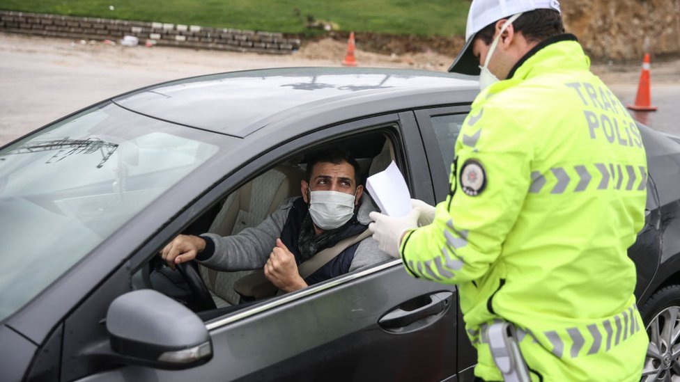 Мужчина в маске проверяет бумагу у полицейского возле своего автомобиля