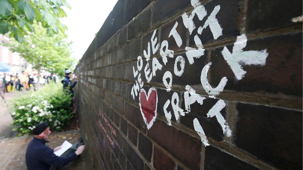 Протестующий (демонстрант) пишет сообщения на стене мелом во время демонстрации в Англии