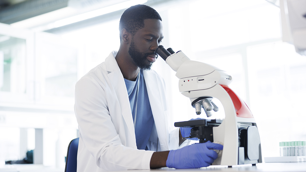 Un científico mirando por un microscopio en un laboratorio.