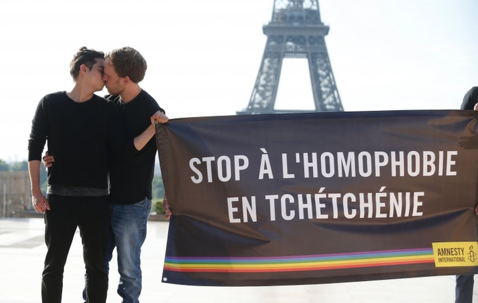 Активисты Amnesty International целуются друг с другом и держат плакат с надписью «Остановить гомофобию в Чечне», чтобы осудить преследование ЛГБТ-сообщества в Чечне 29 мая 2017 года перед Эйфелевой башней в Париже