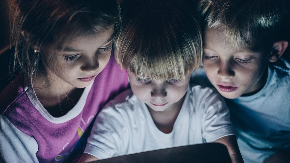 Tres niños mirando una pantalla.