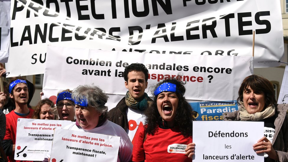 Люди держат плакаты с надписью «встань на защиту разоблачителей» во время демонстрации перед зданием суда в Люксембурге