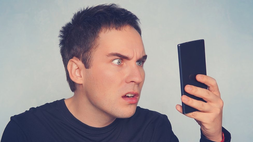 Hombre mirando con ira un celular.
