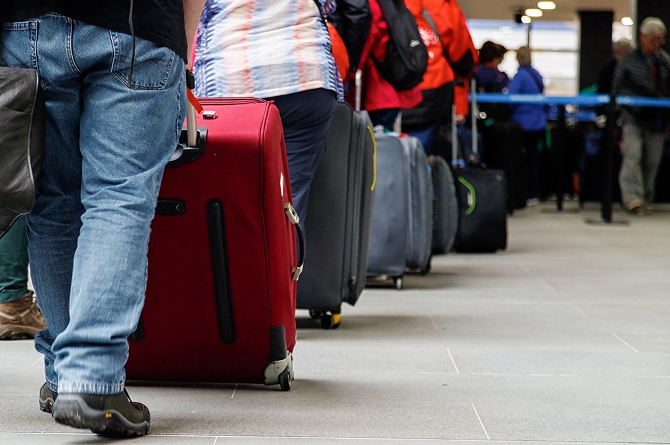 Pessoas com malas em fila de aeroporto