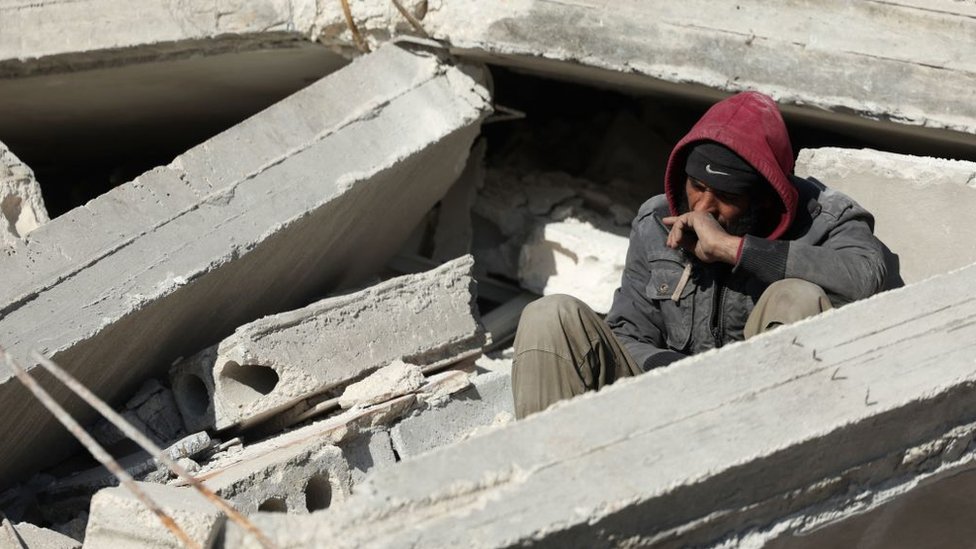 Un hombre sentado sobre los escombros, mientras espera noticias sobre su familia sepultada