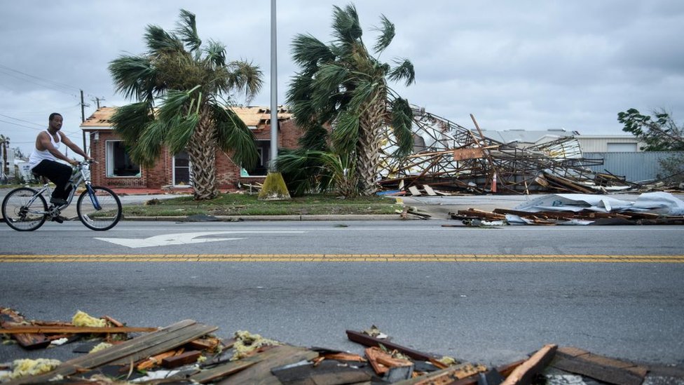 Hombre montando en bicicleta en una calle con casas destruidas por cuenta del huracán Michael.