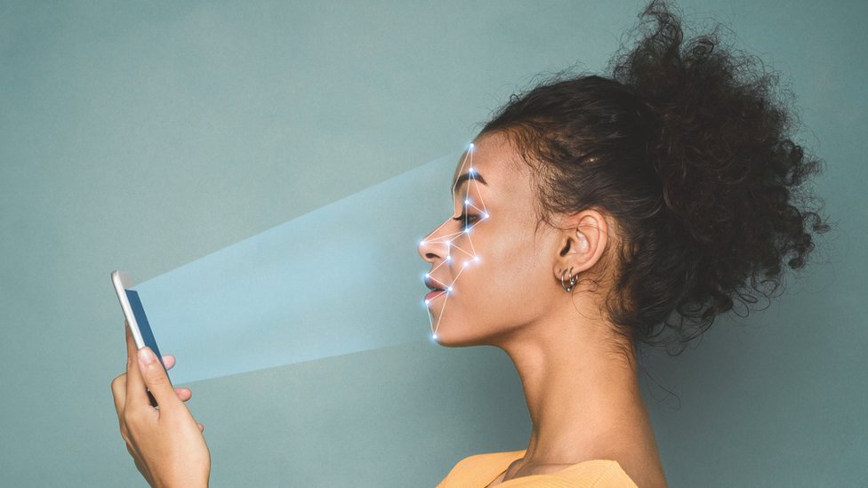 Женщина держит телефон перед собой, пока он сканирует ее лицо точками света на этой комбинации фотоиллюстрации