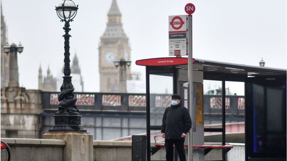 Un hombre con mascarilla en una parada de bus en Londres.
