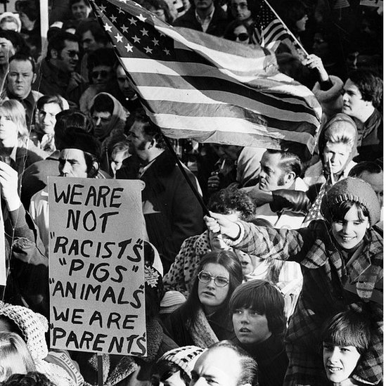 Белые люди протестуют против движения автобусов в Бостоне 1974 г.
