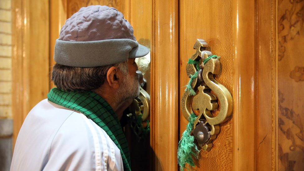 Мужчина целует закрытую дверь храма Фатима Масуме в Куме