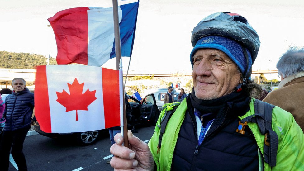 A man holds a stick with the Canada and France flags