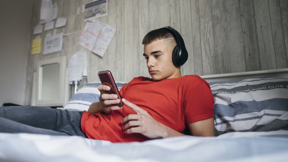 Подросток смотрит в свой телефон, лежа на кровати
