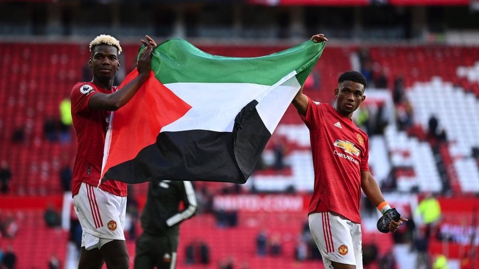 Manchester United's French midfielder Paul Pogba (L) and Manchester United's Ivorian midfielder Amad Diallo (R) carry a Palestinian flag as they walk around the pitch at the end of the game during the English Premier League football match between Manchester United and Fulham at Old Trafford in Manchester, north west England, on May 18, 2021. -